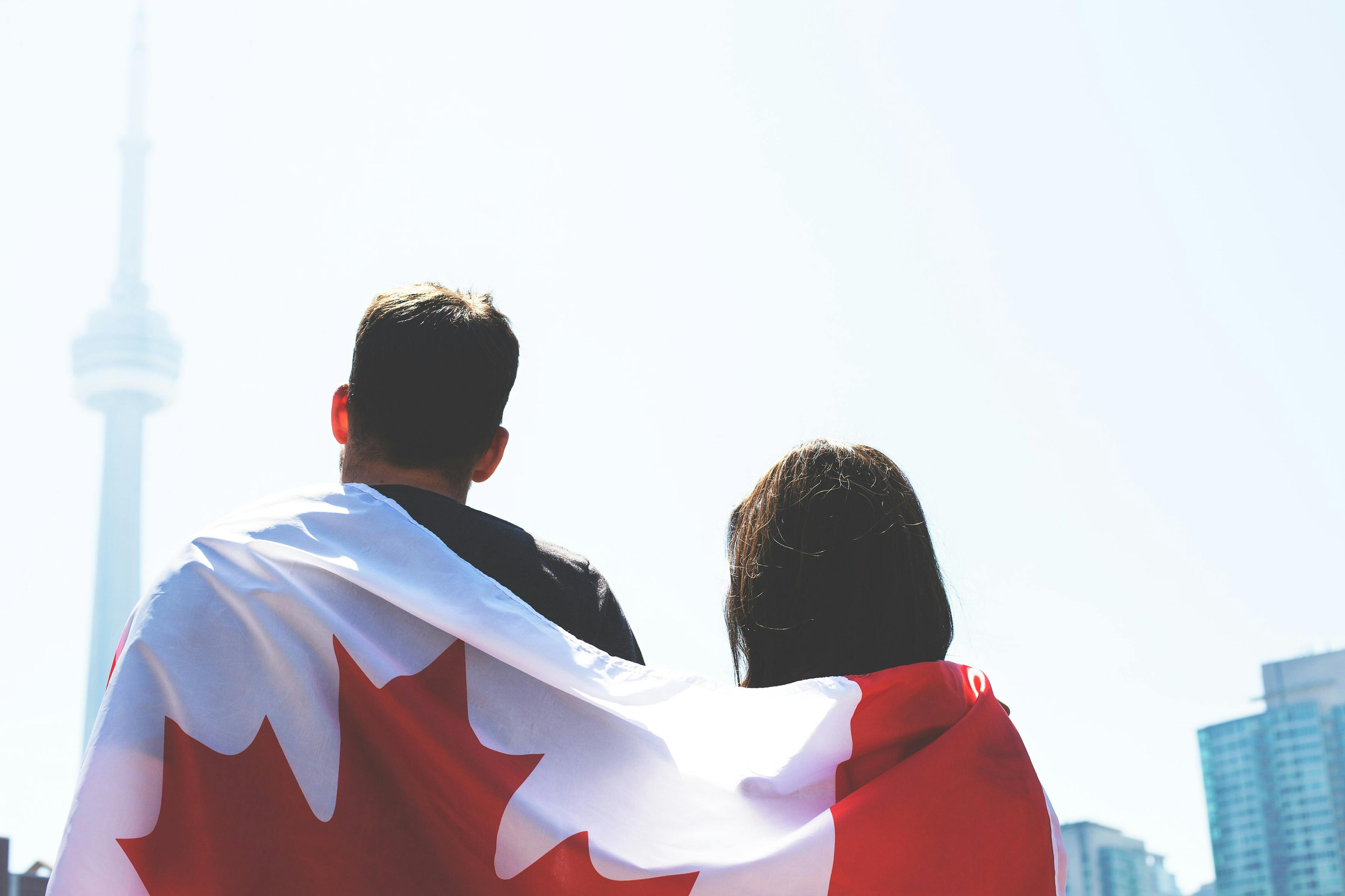 Un drapeau du Canada sur le dos d'un couple de dos regardant la tour CN de Toronto